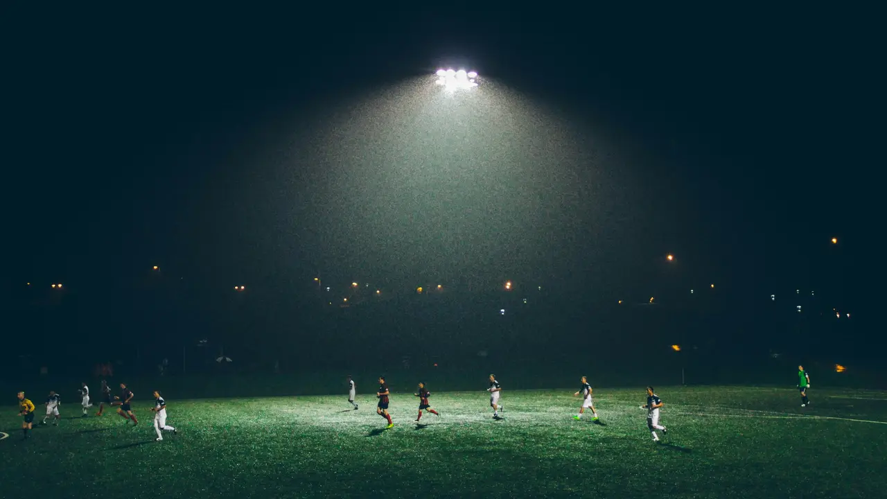 A football pitch at night under a single floodlight, with players on it